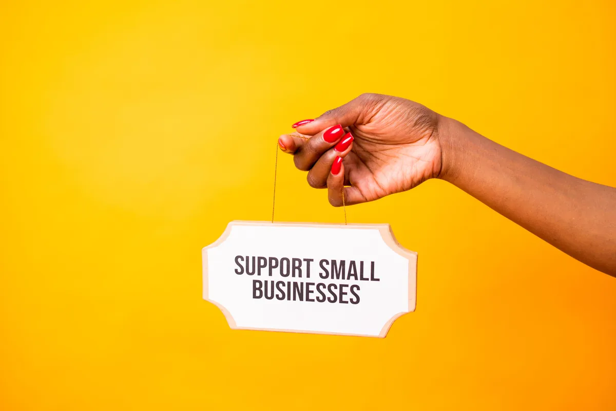 Hand holding a Support Small Businesses sign against a vibrant yellow background, promoting local commerce.